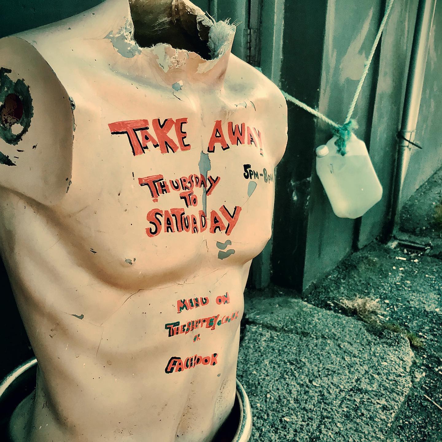 A headless mannequin torso with red-painted text advertising “Take Away Thursday to Saturday” and “Menu on thewhitehouse.ca Instagram” stands on a sidewalk next to a hanging plastic jug, promoting Sheppey takeaways.