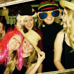 Six smiling women pose together in a photo booth, wearing colorful wigs, hats, and oversized glasses. They appear to be having fun at a New Years Eve 2019 party, laughing and looking at each other. Six smiling women pose together in a photo booth, wearing colorful wigs, hats, and oversized glasses. They appear to be having fun at a New Years Eve 2019 party, laughing and looking at each other.