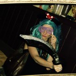 A person in a blue wig, large pink shutter shades, and Minnie Mouse ears poses playfully with a toy scimitar inside a vintage-style photo frame at a lively 2019 New Years Eve party or themed event. A person in a blue wig, large pink shutter shades, and Minnie Mouse ears poses playfully with a toy scimitar inside a vintage-style photo frame at a lively 2019 New Years Eve party or themed event.