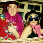 Two people pose playfully wearing colorful feather boas and fun accessories at a lively 2019 New Years Eve celebration. One gives a thumbs up in a red tropical shirt and multicolored hat; the other sports star-shaped glasses, both smiling in a framed setting. Two people pose playfully wearing colorful feather boas and fun accessories at a lively 2019 New Years Eve celebration. One gives a thumbs up in a red tropical shirt and multicolored hat; the other sports star-shaped glasses, both smiling in a framed setting.