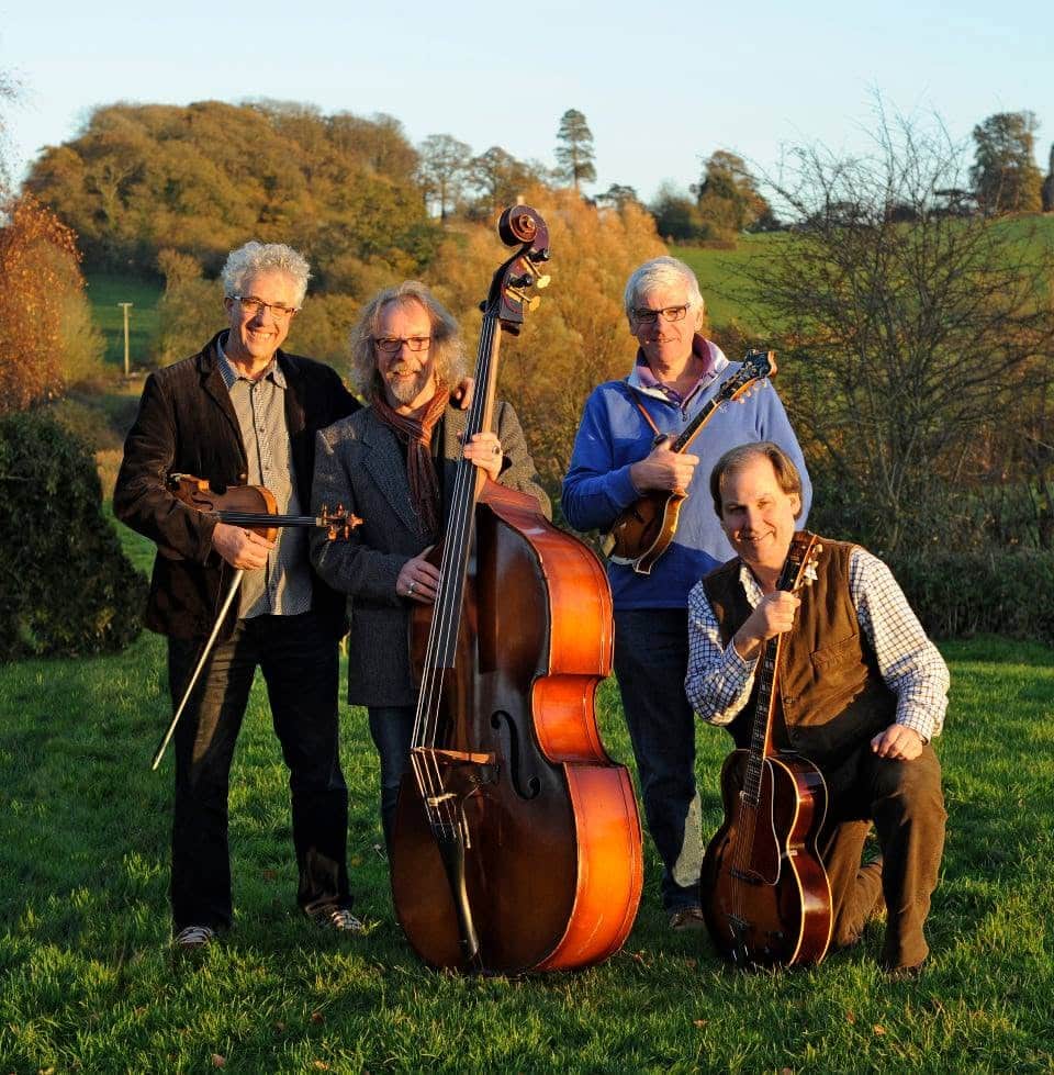 Old Boston tea party photo of the band holding instruments in a field with trees in the background.