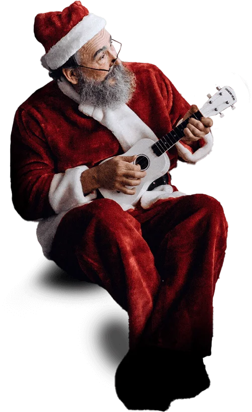 A man dressed in a Santa Claus outfit, with a white beard and glasses, sits while playing a small white ukulele.